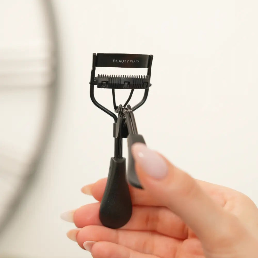 LIFT® Lash Curler by Beauty Plus held in hand, showing the matte black handles and lash guide detail.