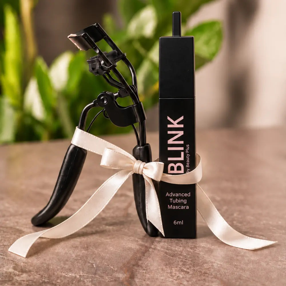 The Lash Duo by Beauty Plus, BLINK® Advanced Tubing Mascara 6ml and LIFT® lash curler tied together with a cream satin ribbon on a marble surface.
